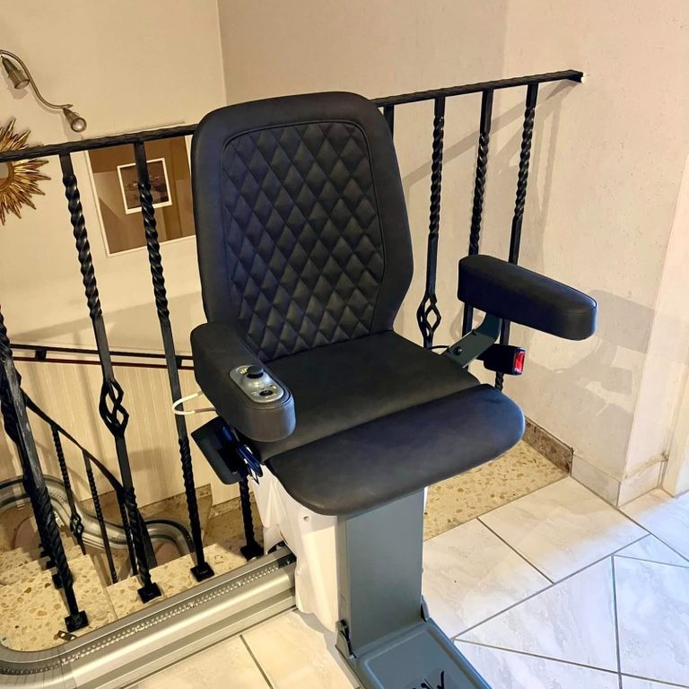 Treppenlift mit schwarzem Sitz und Armlehnen, montiert an einer Treppe. Treppenlift mit schwarzem Sitz und Armlehnen, montiert an einer Treppe.